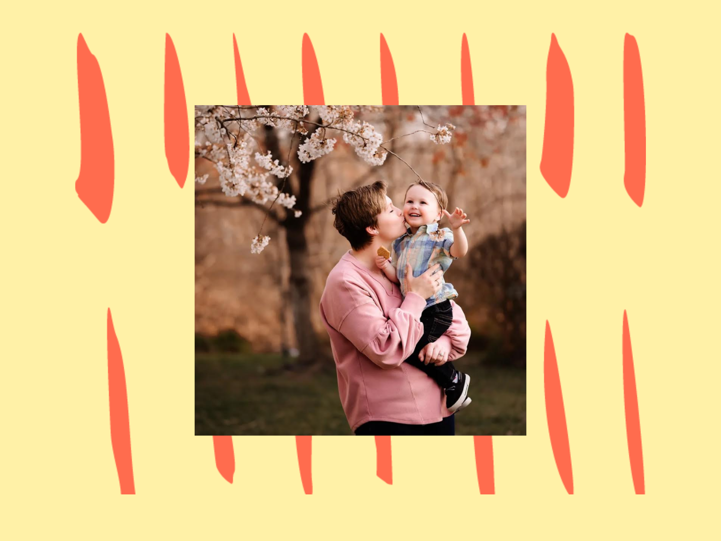 Falon holds her one-year-old son, giving him a kiss on the cheek, under a blossoming tree