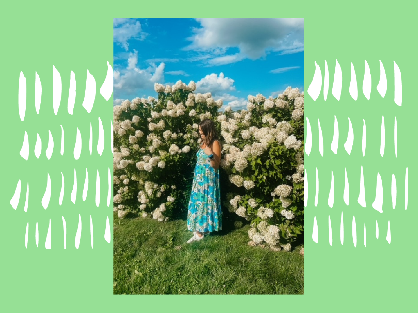 Rebecca poses in a long teal dress, smiling, in front of bushes of flowers.